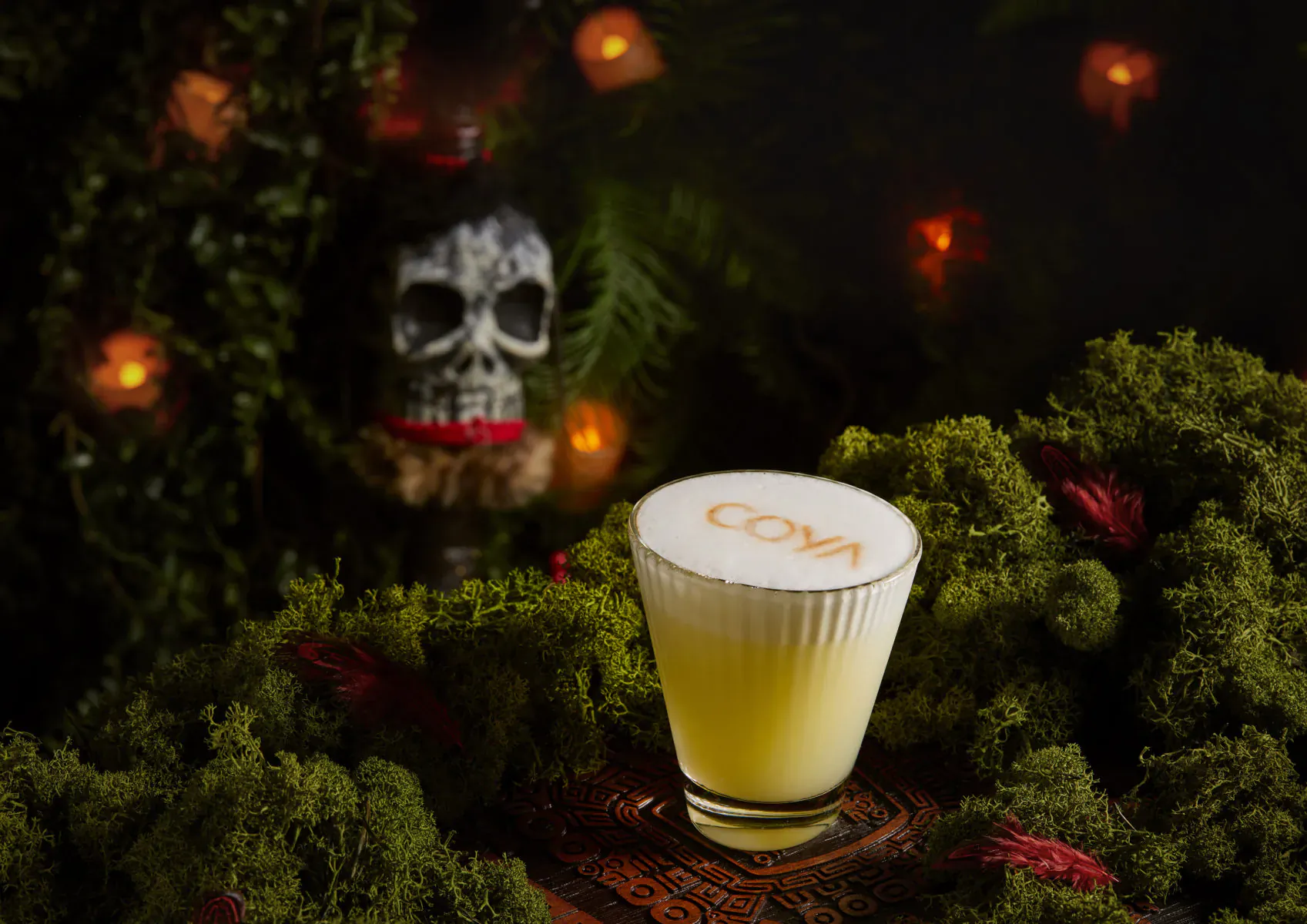 COVA cocktail in yellow foam glass amid Halloween skull, ferns, and warm lights in Wonderland setting