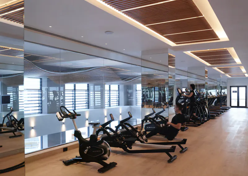 Modern gym at Angsana Corfu Resort with spin bikes, mirrors, wood ceiling, and person exercising