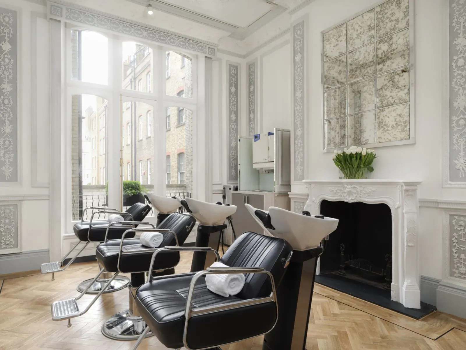 Elegant Philip Kingsley hair clinic interior with black salon chairs at white wash basins near ornate fireplace