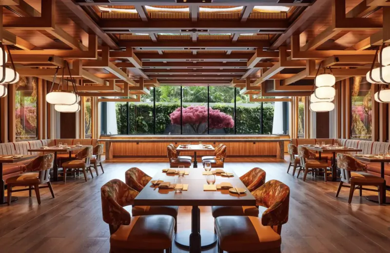 Elegant wooden-beamed dining room at Paiza Collection with large windows, pink flowering tree, leather chairs, and tables.