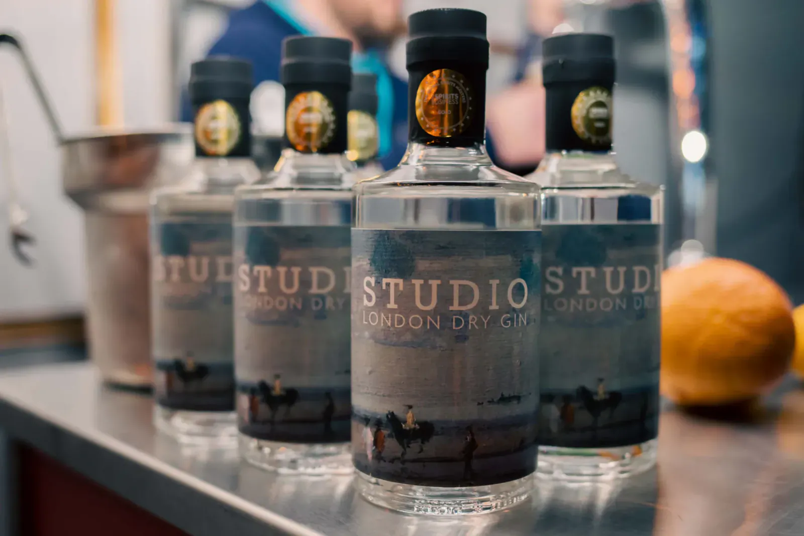 Several bottles of Studio London Dry Gin on a counter with ice bucket and orange, summertime vibe.