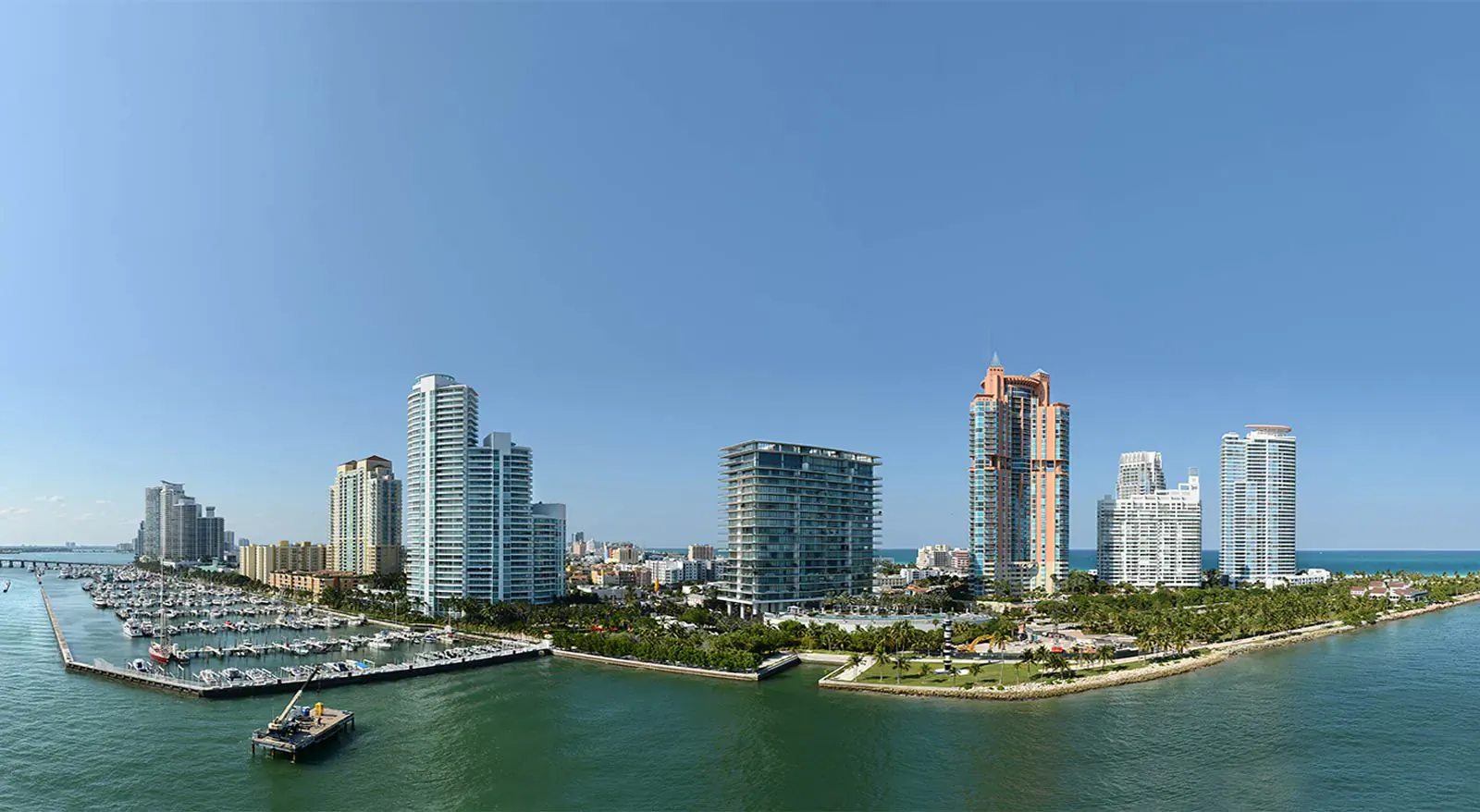 Panoramic view of Miami skyline with high-rise condos, marina with yachts, and turquoise bay under clear blue sky