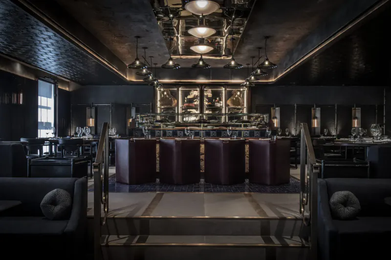 Elegant dark interior of Lucky Cat Mayfair restaurant with ornate bar, purple stools, pendant lights, and tables.