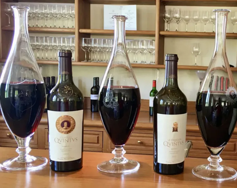 Four elegant decanters with red wines like Caymus and Conundrum on wooden bar shelf.
