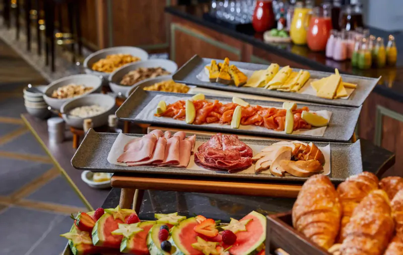 Hotel Indigo Chester breakfast buffet with croissants, cold cuts, cheeses, fruits, and pastries on wooden counter.
