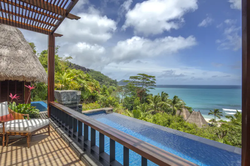 Anantara Seychelles thatched villa balcony with infinity pool, lounge chairs, overlooking tropical ocean bay and hills.