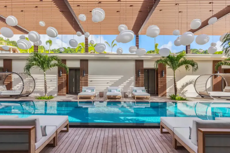 Silversands Grenada luxury poolside gallery with turquoise pool, loungers, palms, and white pendant lamps under wooden ceiling