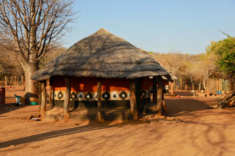 Traditional round thatched hut with red walls and black geometric patterns at Elephant Camp lodge, Zimbabwe, in savanna setting.