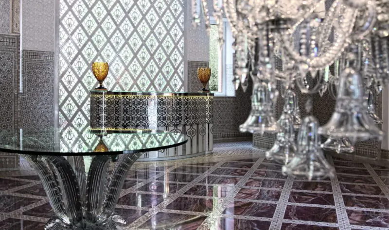 Opulent hotel lobby in Royal Mansour Marrakech with crystal chandelier, glass table, gold vases, and ornate walls.