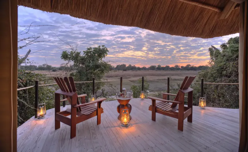 Two wooden Adirondack chairs with lanterns around a terracotta pot on a deck overlooking savanna at sunset in Lion Camp.