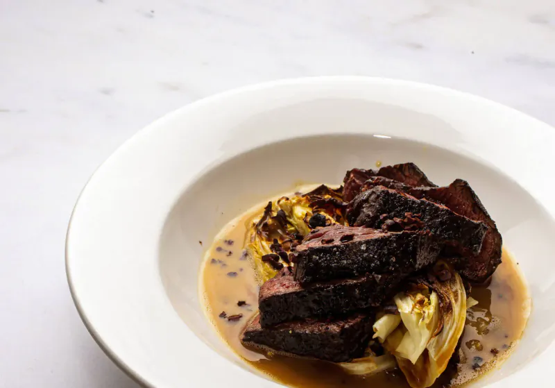 White bowl with seared beef slices, roasted fennel, and peppercorn sauce on marble surface