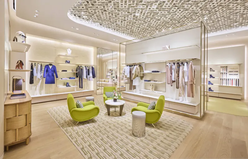 Louis Vuitton store interior at Heathrow with clothing displays, green armchairs, and modern ceiling design.