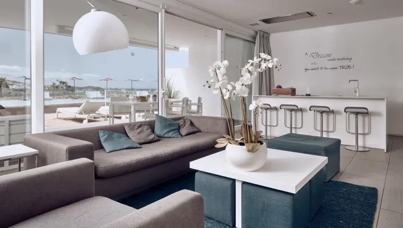Modern Baobab Suites living room with grey sofas, white orchids on table, bar stools, and sea view terrace in Tenerife resort.