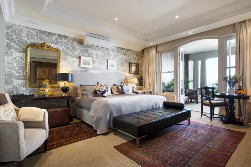 Elegant bedroom at 21 Nettleton Boutique Hotel, Cape Town, with king bed, ornate mirrors, balcony to sea view, and Persian rug.