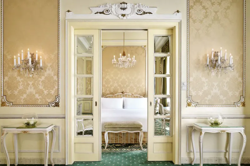 Elegant open double doors to luxurious bedroom with chandelier, candelabras, and floral tables in Hotel Imperial Vienna suite