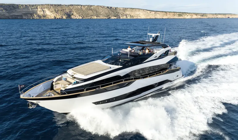 White luxury yacht speeding across blue sea with rocky cliffs in background