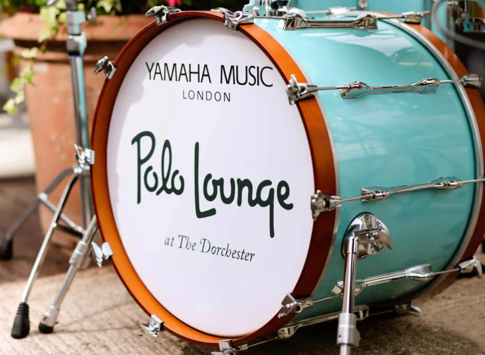 Yamaha Music London drum kit with Polo Lounge at The Dorchester text on turquoise bass drum, outdoors with plants.