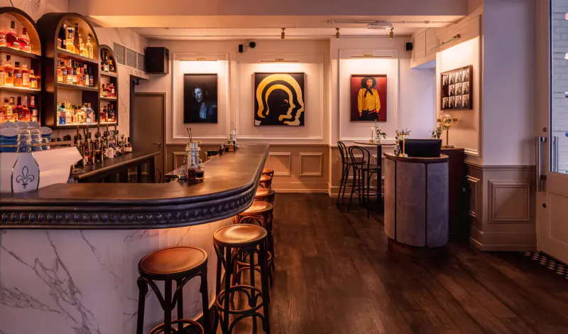 Ziggy Green bar in London: curved wooden bar with leather stools, lit liquor shelves, modern art gallery walls.