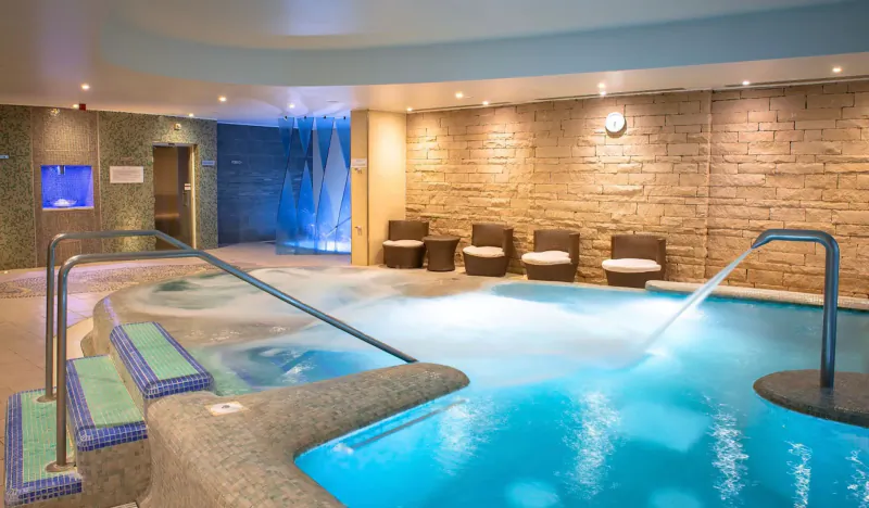 Luxury spa pool with bubbling blue water, steps, wall jets, lounge chairs, and stone walls at Old Course Hotel.