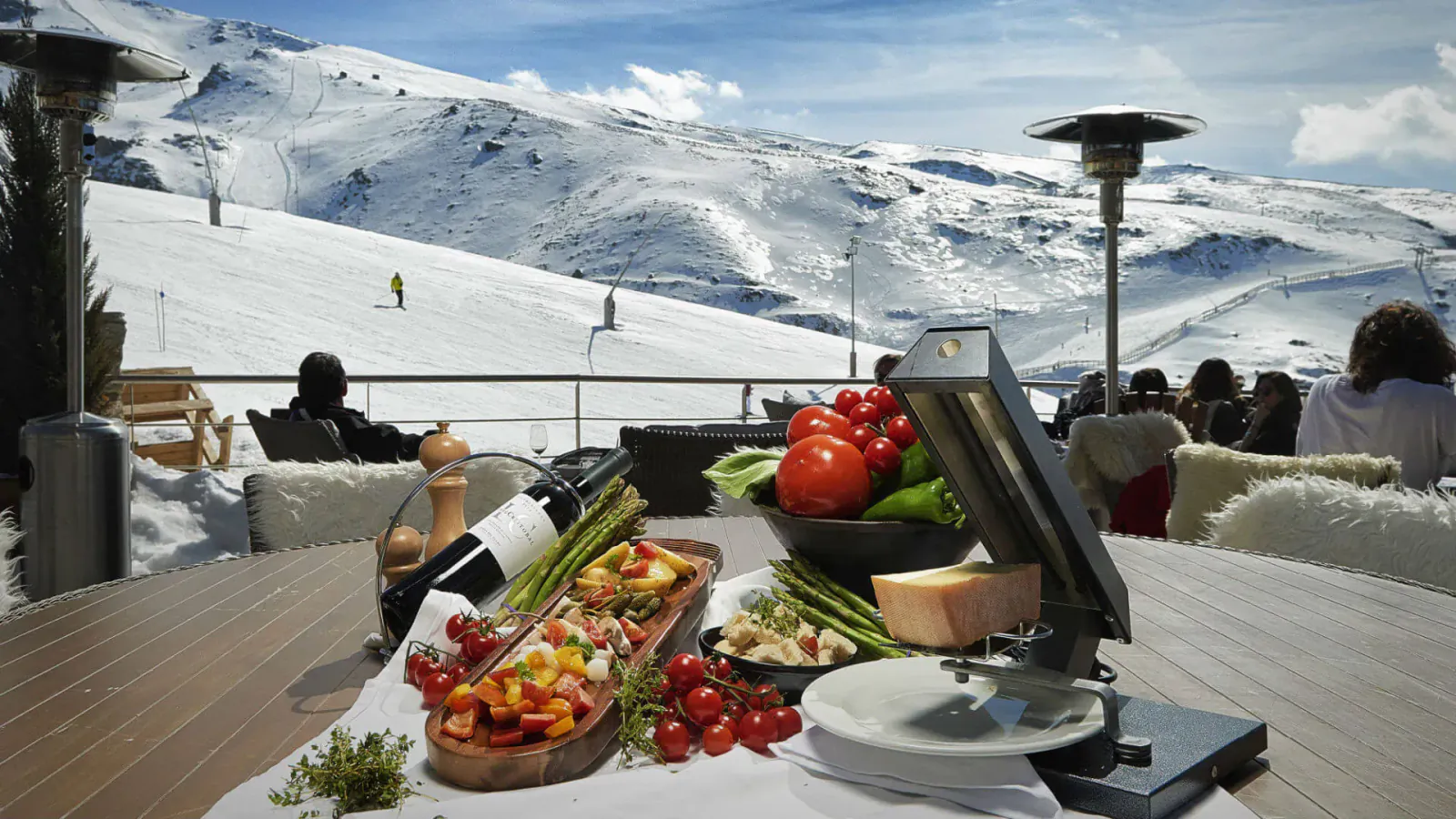 Close-up of antipasti platter with tomatoes, asparagus, cheese on wooden table at El Lodge, Sierra Nevada ski resort with snowy mountains.