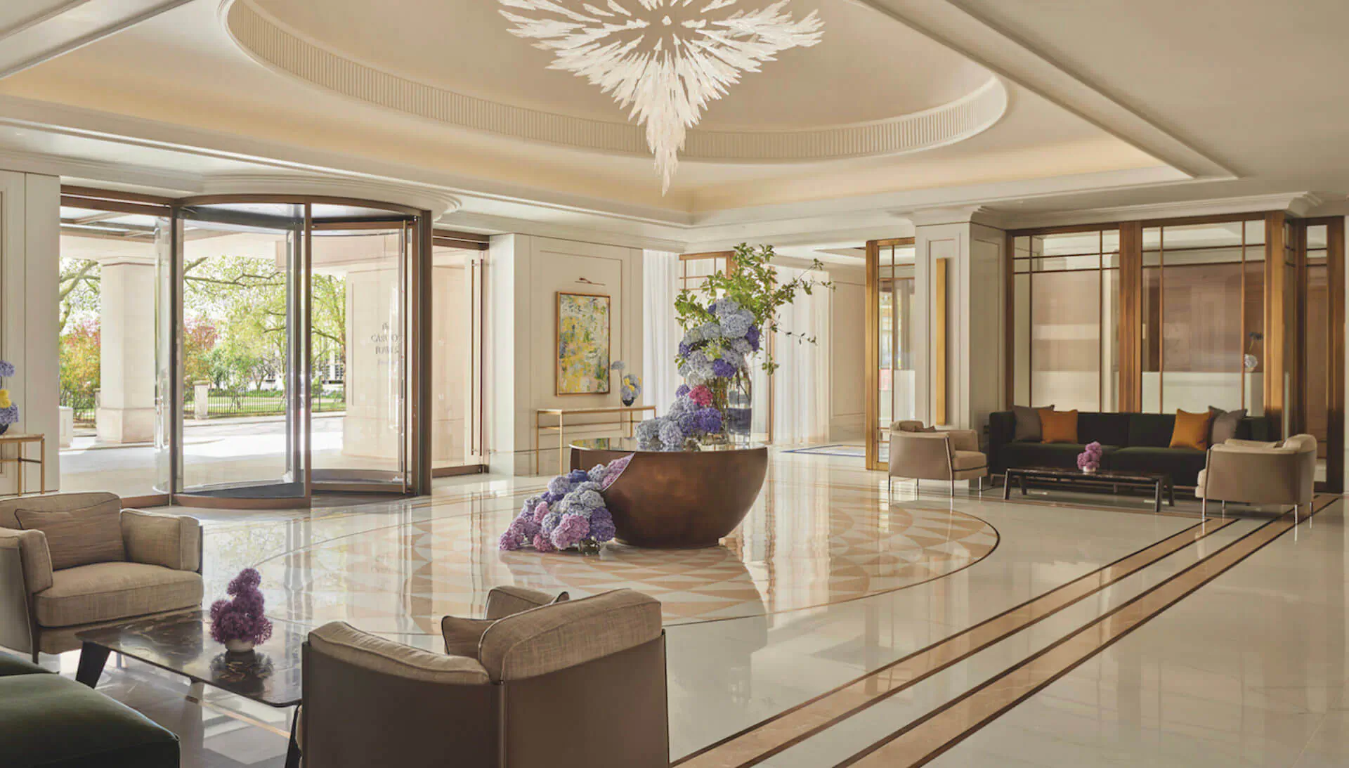 Elegant Carlton Tower Jumeirah hotel lobby with chandelier, purple floral arrangements, plush seating, and garden view entrance.