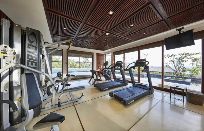 Modern gym in Ani Private Resorts with Cybex weight machine, treadmills, wood ceiling, large windows to tropical view.