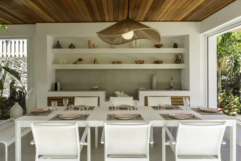 Modern white dining table with chairs in Villa Diamond, Mauritius beach villa, rattan lamp, shelves with ceramics, tropical garden view
