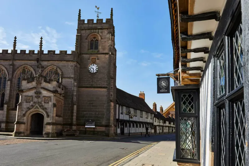 Gothic church tower with clock beside timber-framed buildings and pub sign in historic Stratford upon Avon street