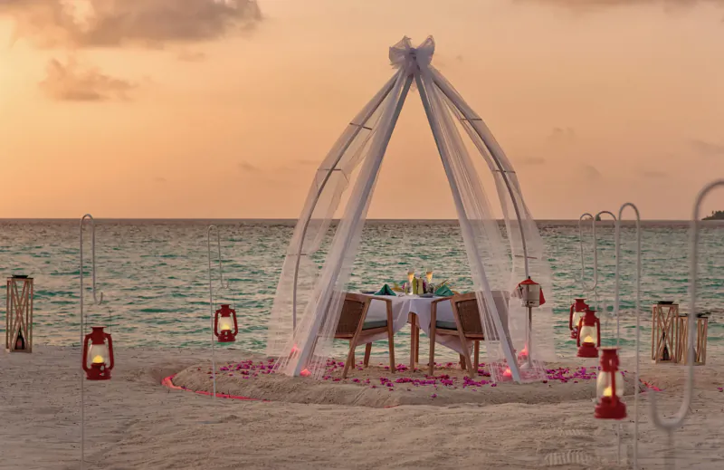 Romantic candlelit beach dinner for two under white gauze canopy at sunset, Amari Raaya Maldives, with lanterns and ocean view.