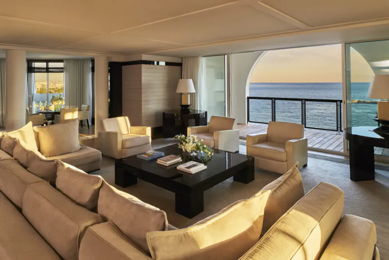 Luxurious living room with beige sofas, coffee table, lamps, and sunset ocean balcony view.