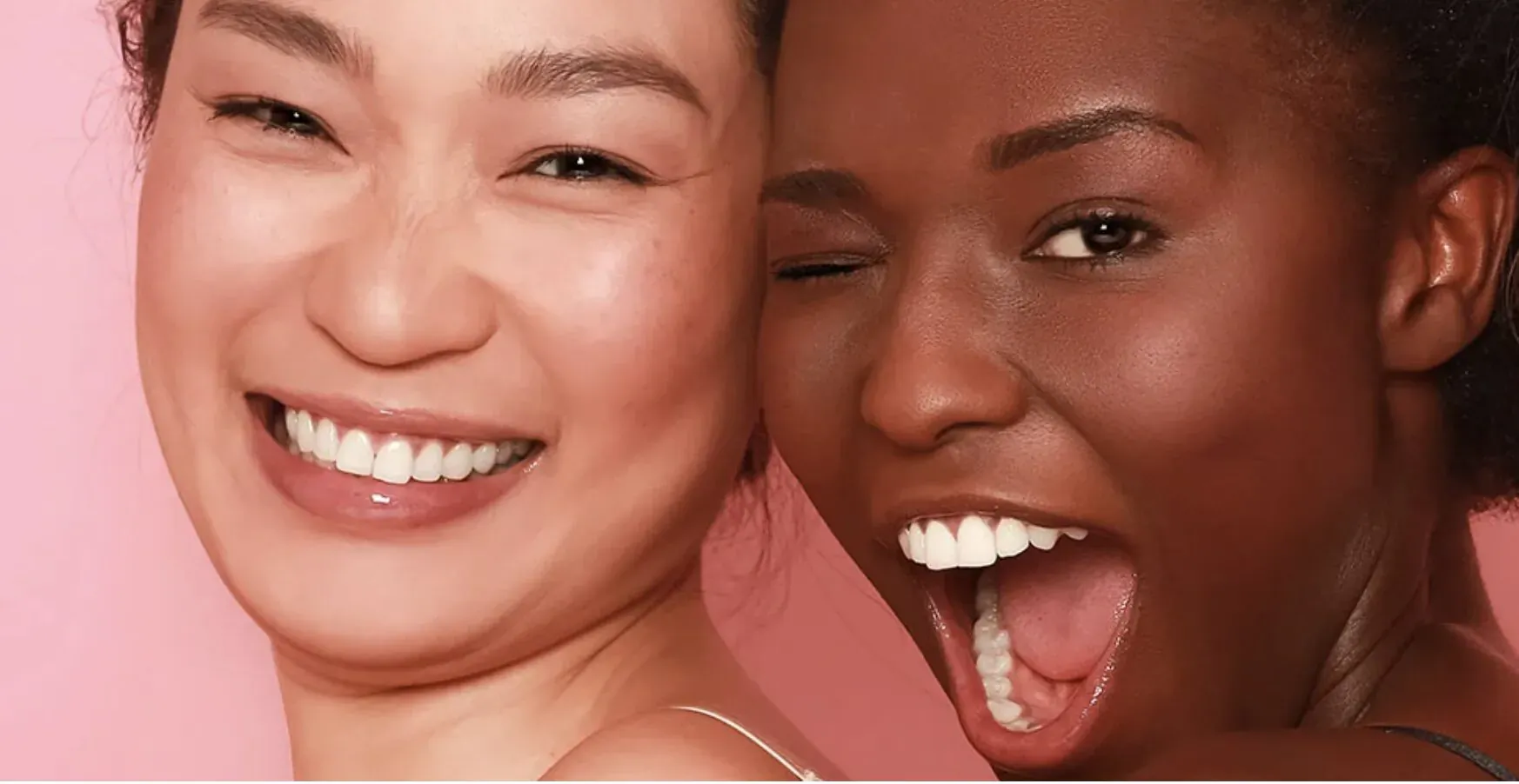 Asian and Black women smiling joyfully side by side against pink background
