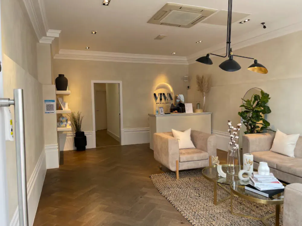 Elegant VIVA Skin Clinics reception with beige sofas, glass coffee table, plants, and front desk.