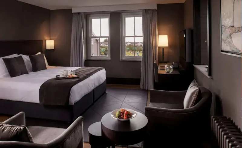 Elegant hotel room at Twr y Felin with king bed, tray of fruit, armchairs, lamps, and garden window view.