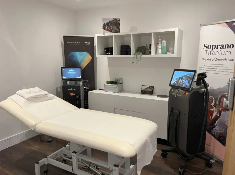 Modern clinic room with Soprano Titanium laser, treatment bed, screens, and 'Art of Smooth Skin' poster at Aqua-Tox Wellness Clinic