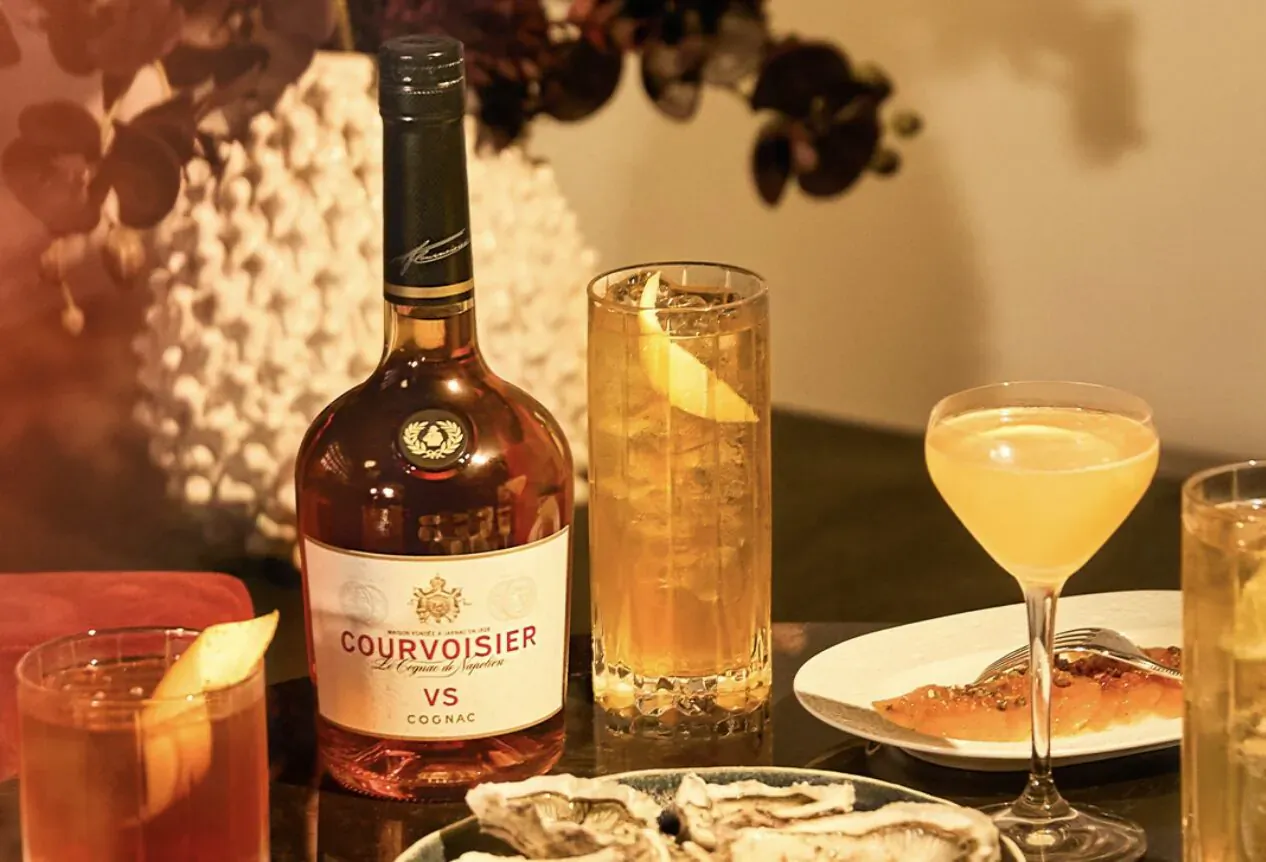 Courvoisier VS bottle with highball lemon iced tea, lemon drop cocktail, and oysters on plate
