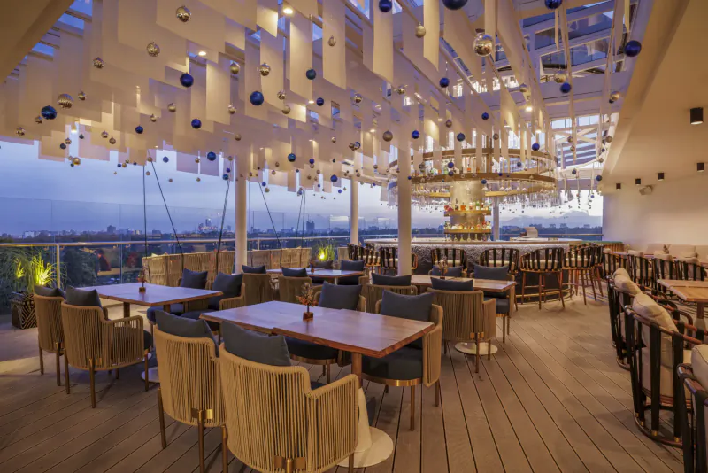 Elegant rooftop bar at Gem Forest Hotel, Nairobi, with rattan furniture, blue ornaments, lit chandelier, bar, and city skyline at dusk.