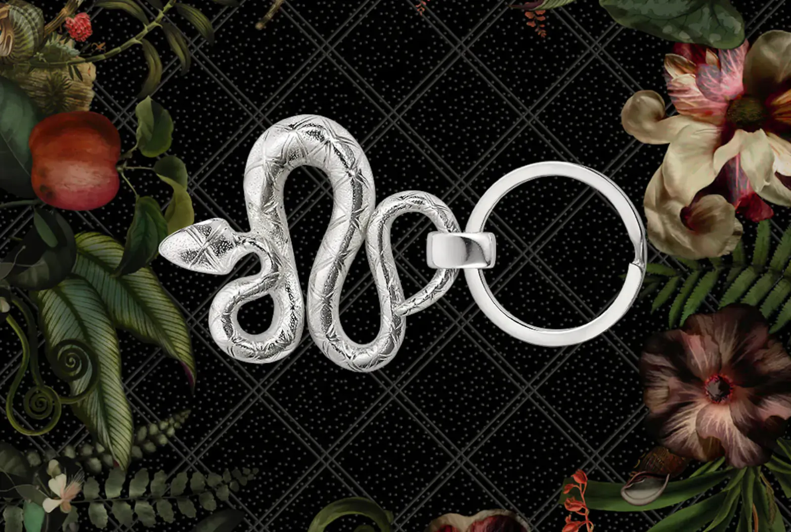 Silver coiled snake keyring with ring, framed by black lattice and Jardin d’Éden floral motifs