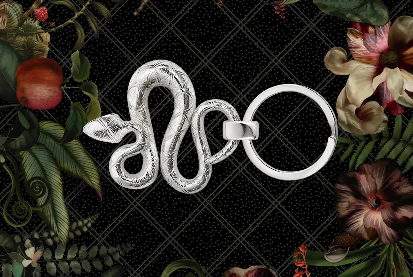 Silver coiled snake keyring with ring, framed by black lattice and Jardin d’Éden floral motifs