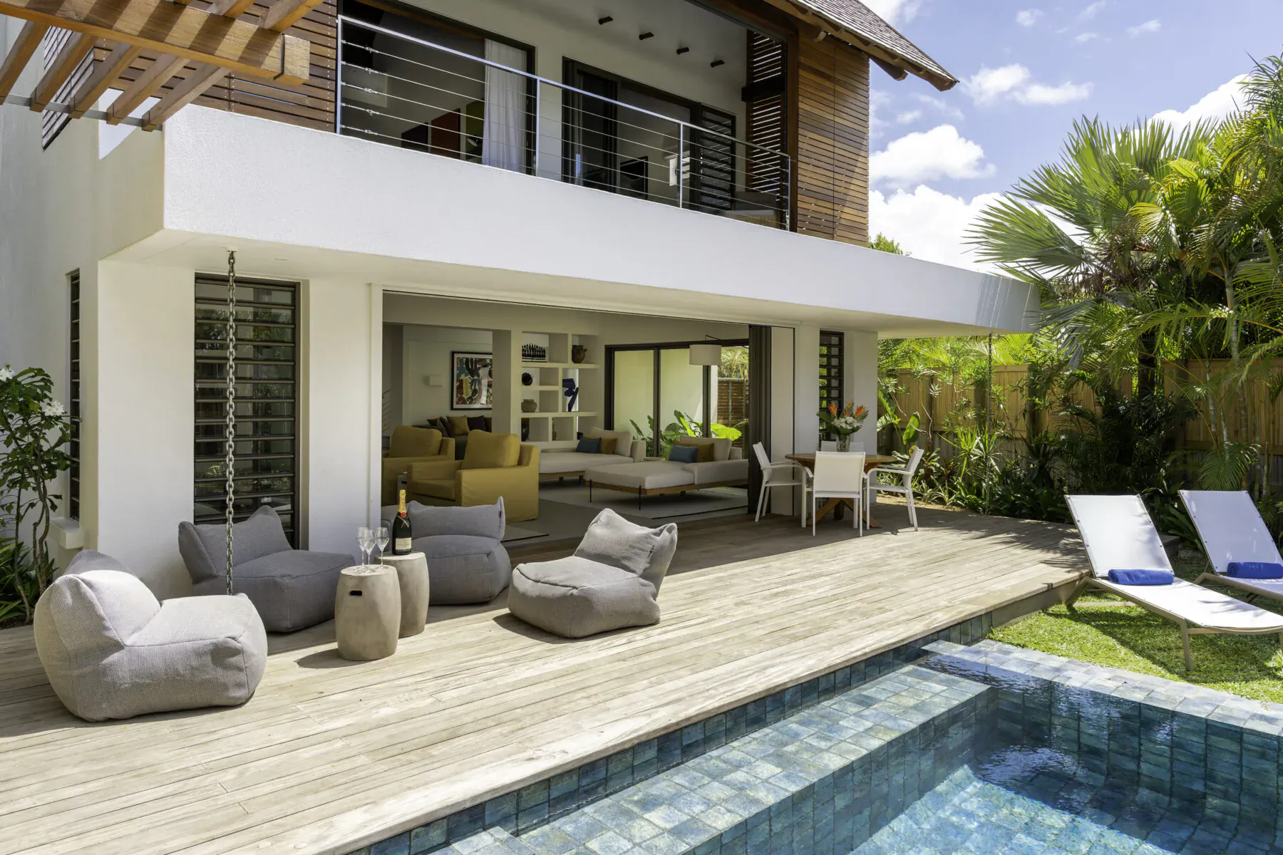 Modern white Villa Diamond in Mauritius with wooden deck, gray bean bags, lounge seating, infinity pool, and palm trees.