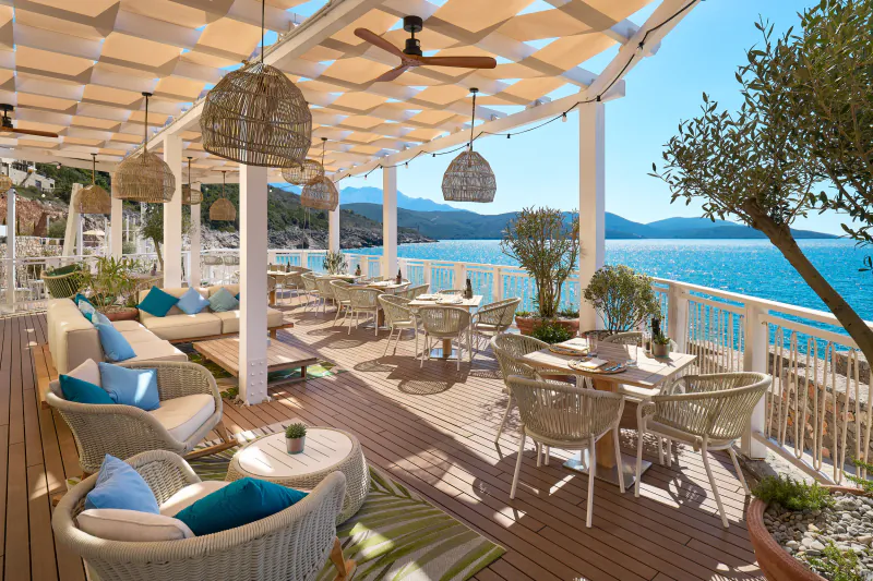 The Chedi Luštica Bay: Outdoor terrace dining with white wicker furniture, pendant lamps, olive trees, and Adriatic Sea view.