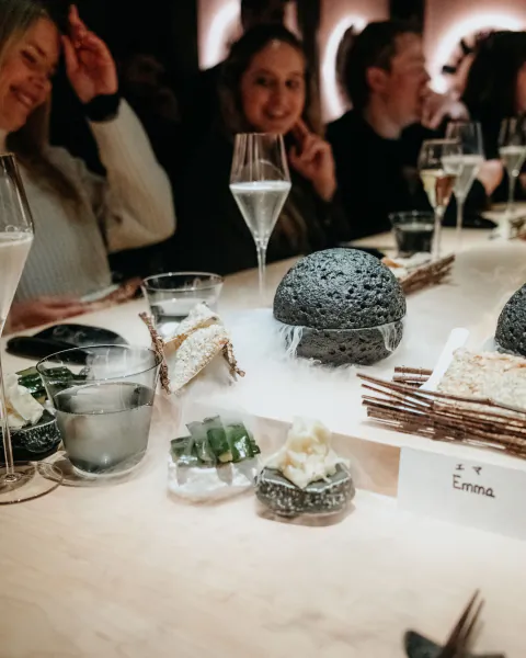Emma Blunt dines at LUNA Omakase: smiling women at table with black dome dish, champagne flutes, and name card 'Emma'.