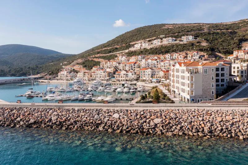 Aerial view of The Chedi Luštica Bay marina in Montenegro, with luxury yachts, white buildings on hills, and turquoise sea.
