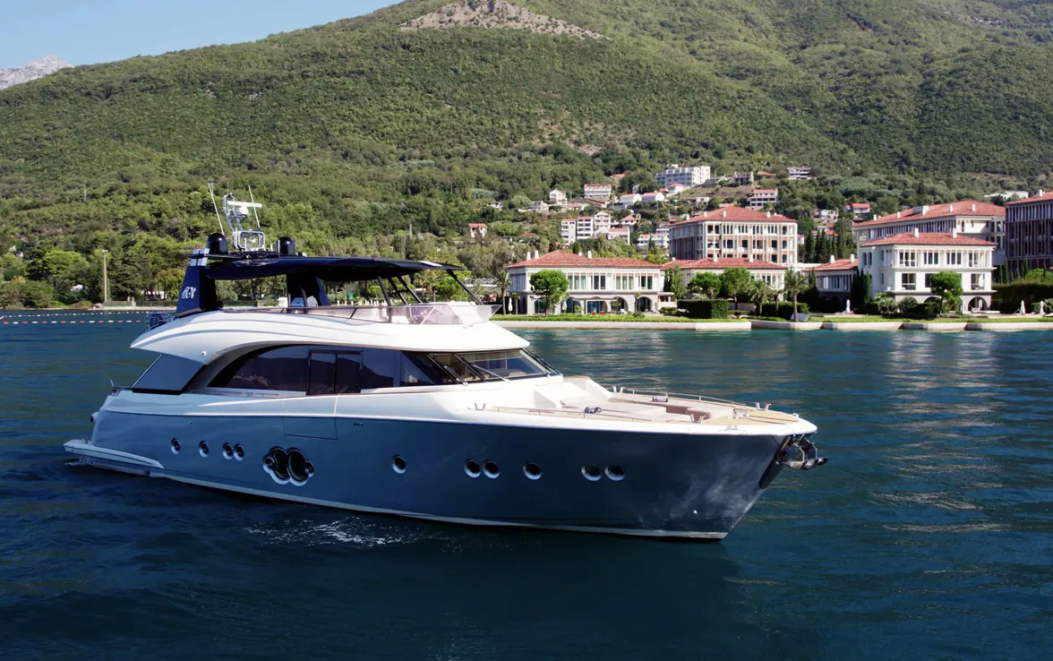 White luxury motor yacht Giorgio cruising on lake with green mountains and red-roofed buildings in background.