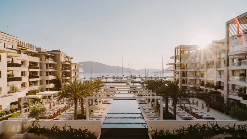 Aerial view of Regent Porto Montenegro luxury resort with infinity pool, palm trees, marina, yachts, and sunset over bay