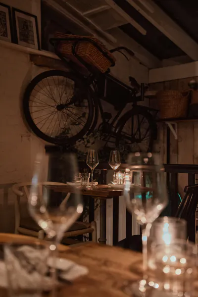 Close-up of two wine glasses and candlelight on wooden table in cozy bistro with hung bicycle and baskets in background