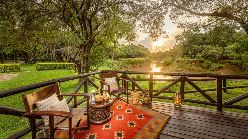 Fairmont Mara Safari Club deck with chairs, table, lanterns on red rug, overlooking river and safari landscape at sunset.