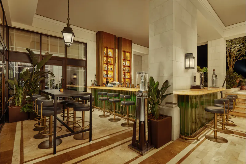 Elegant modern bar at Regent Porto Montenegro with green counters, bar stools, plants, and liquor shelves.