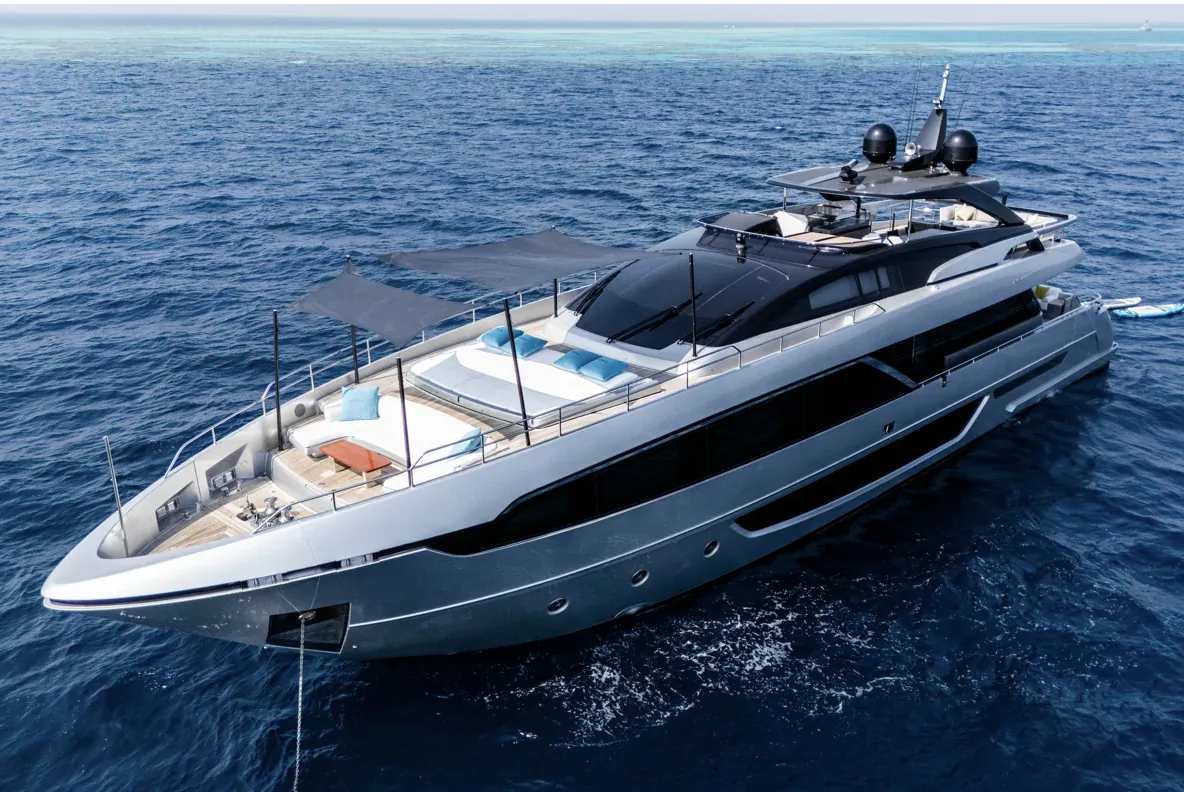 Dark Horse Riva 100 Corsaro luxury yacht with sunshades and loungers on deck, anchored in turquoise ocean.