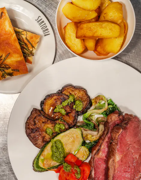 Sartoria plate: roasted beef, grilled aubergine and zucchini with pesto, roasted potatoes, focaccia on metal surface