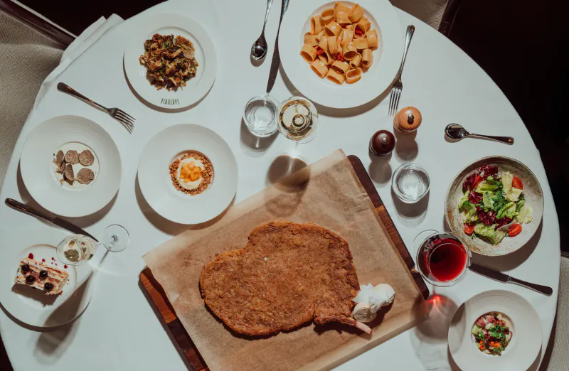 Elegant Italian restaurant table with oversized breaded veal cutlet, pasta, salad, egg, and wine at Sartoria.
